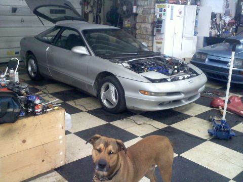 1993 Ford Probe - A silver coupe sits in a garage with its hood open, revealing the engine bay. Another vehicle is parked behind it.
