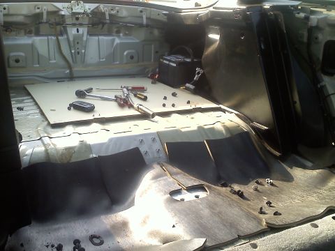 1993 Ford Probe - Bare automobile interior during restoration with floor pan exposed and ratchets, screwdriver and hardware on a removed panel.