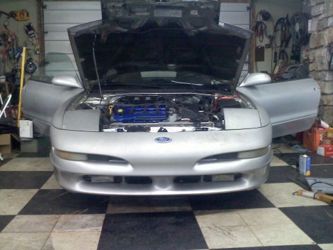 1993 Ford Probe - Silver Ford Probe in a checkered-floor garage with hood up and pop-up headlights raised, blue valve cover visible.