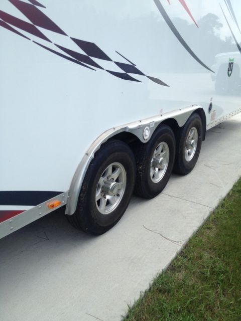 1967 Ford Mustang - A white trailer with a checkered graphic design is shown from the side, focusing on its triple axle wheel setup.