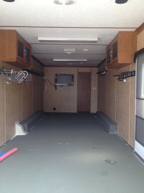 1967 Ford Mustang - Empty cargo trailer interior showing cabinets, a mounted TV, and tie-down anchors on the floor.