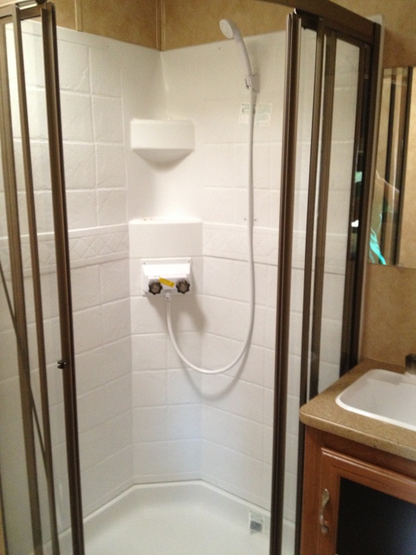 RV shower stall with glass doors, white tiled walls, and a sink vanity next to it