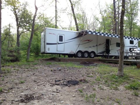 1967 Ford Mustang - A white toy hauler trailer is set up in a campsite with trees surrounding it.