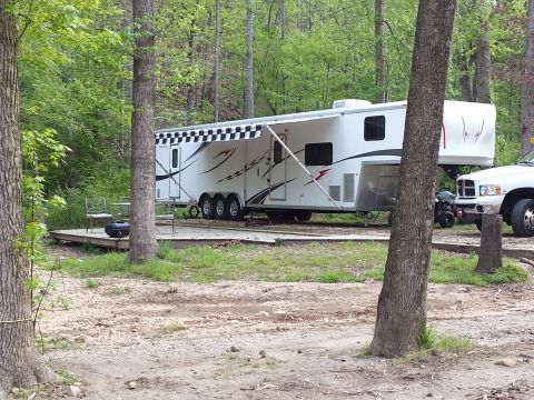1967 Ford Mustang - A white fifth wheel trailer is set up at a campsite, with a pickup truck parked nearby. The trailer features a checkered awning and racing-…