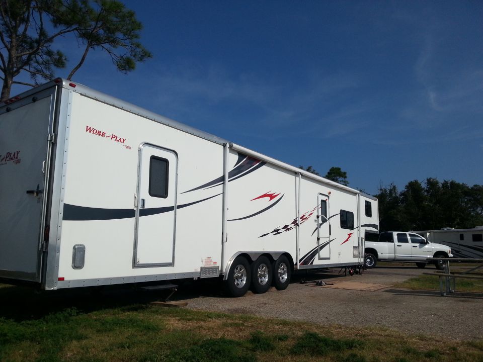 White toy hauler trailer with 'Work and Play' graphics parked next to a white pickup truck