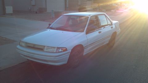 1993 Mercury Tracer - A white 1993 Mercury Tracer sedan is parked on a street with the sun setting behind it.