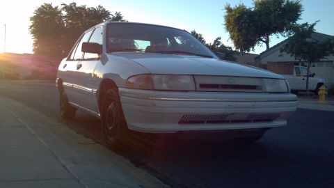 1993 Mercury Tracer - A white 1993 Mercury Tracer sedan is parked on a residential street during sunset.