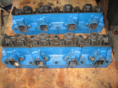 1963 Ford Galaxie - Two blue engine cylinder heads are displayed on a wooden surface, showing their intake and exhaust ports.
