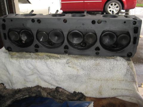 1963 Ford Galaxie - Engine cylinder head with valves, placed on a towel with a red vehicle in the background.