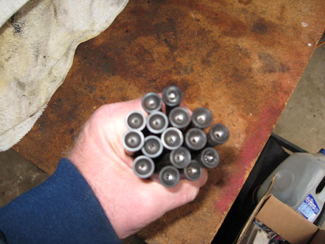 Hand holding a bunch of metal valve lifters. A white cloth is to the left, and a workbench surface is visible