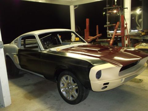 1967 Ford Mustang - A 1967 Ford Mustang coupe is shown in a garage, partially painted and undergoing restoration work.