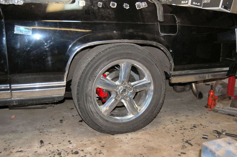 Rear wheel with chrome rims and red brake calipers on a black car. Chrome trim along the lower body