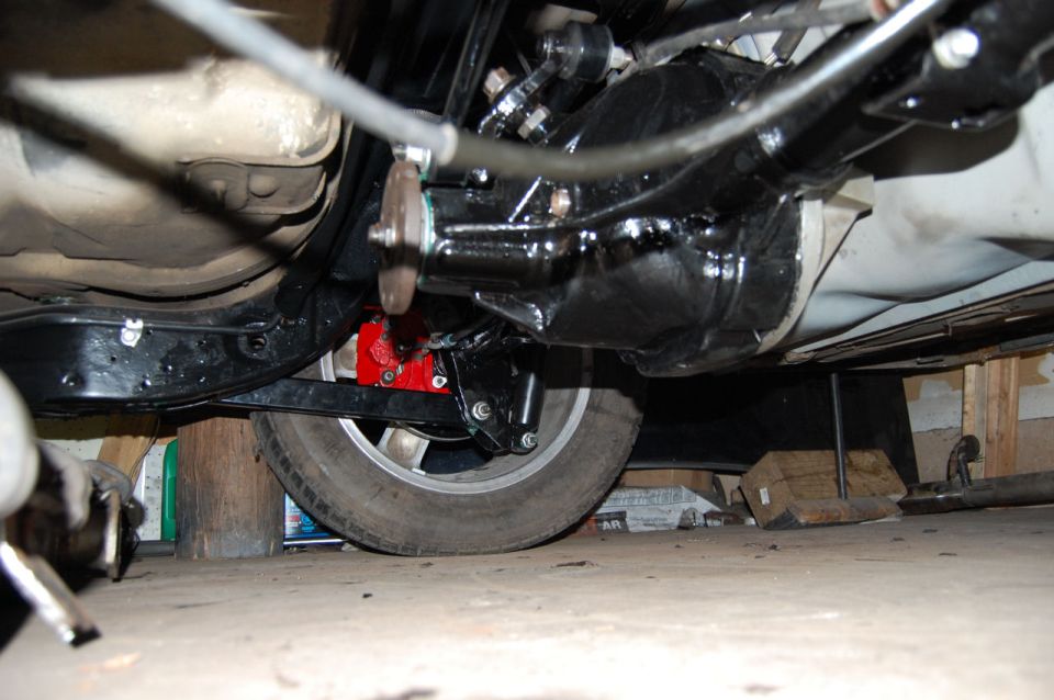 Underside of a vehicle showing a black rear axle assembly with red brake calipers and a silver wheel