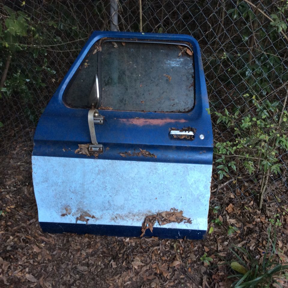 Blue and light blue two-tone Ford truck door, rusted and weathered, lying on the ground