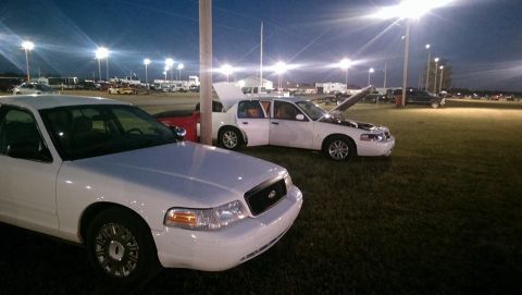 2000 Mercury Grand Marquis - Two white sedans are parked on a grassy field under bright lights at dusk.