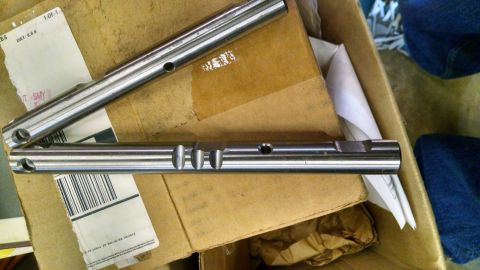 1979 Ford F-150 - Two metal shafts with machined features are shown resting on cardboard packaging.