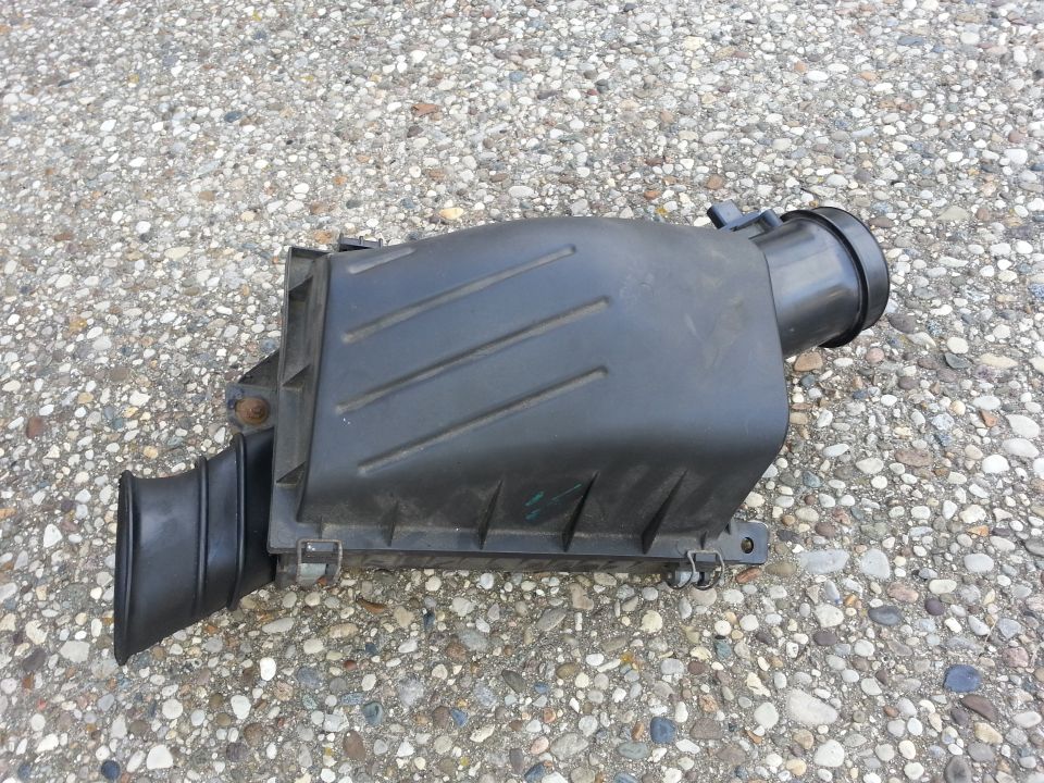 Black plastic air filter airbox housing removed from car, sitting on concrete