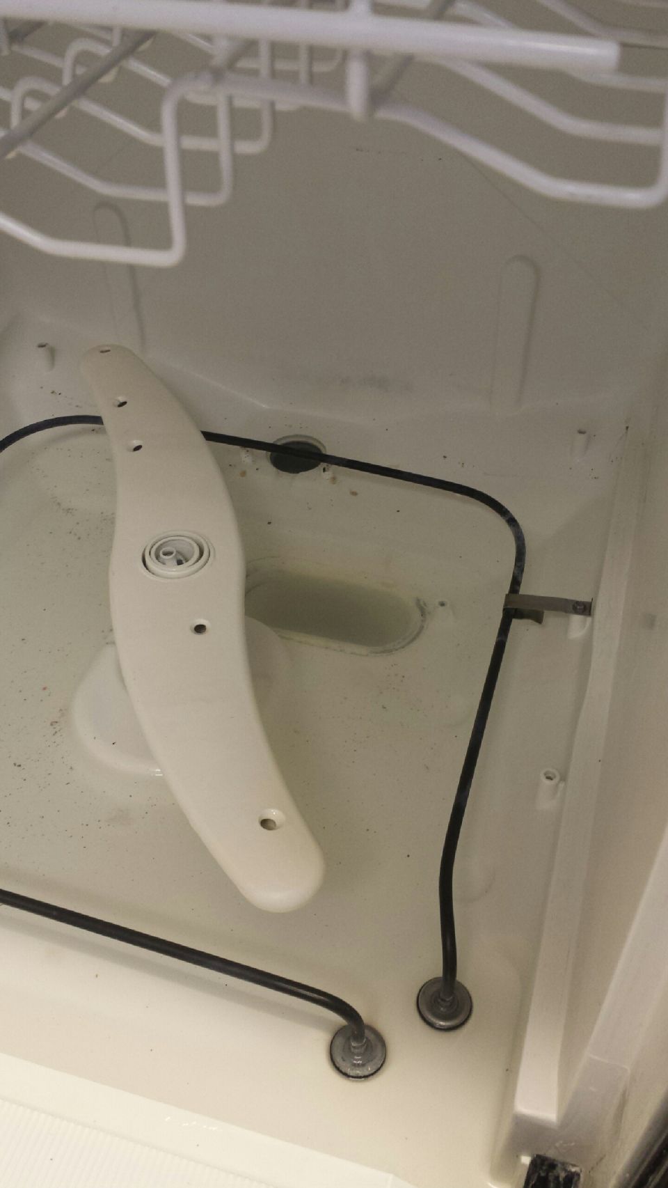 Dishwasher interior with a white spray arm, black hoses, and a dirty basin