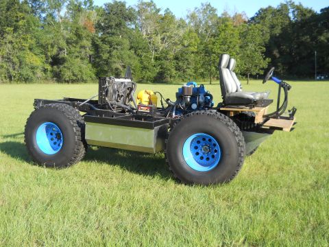 1992 Ford Bronco - This custom-built vehicle chassis features large tires and exposed mechanical components, sitting in a grassy field.