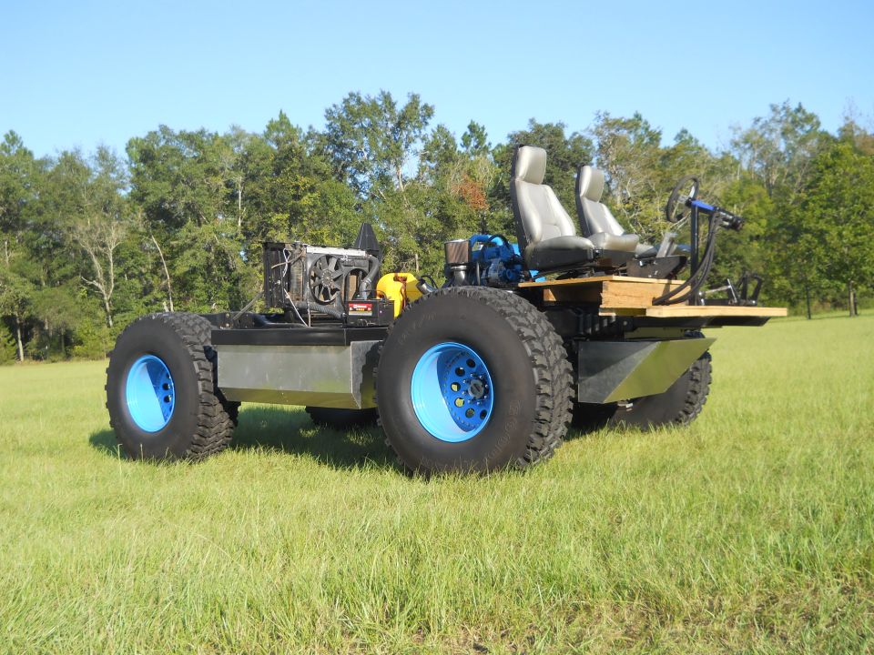 Amphibious all-terrain vehicle with large blue-rimmed tires, dual seats, and exposed engine components, parked on a grassy field