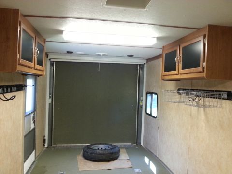 1967 Ford Mustang - The interior of a cargo trailer features overhead cabinets, a spare tire on the floor, and a large rear door.