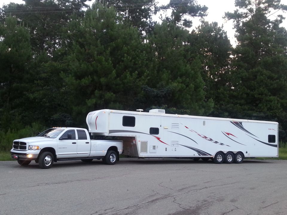 White Dodge Ram pickup truck towing a large white gooseneck trailer with red and black graphics