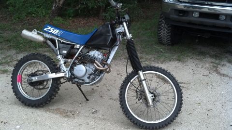 1995 Ford Bronco - A dirt bike with a blue seat and "250R" visible on the side is parked outdoors next to a large truck.