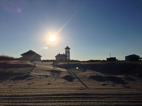 1979 Ford Bronco - A sunny day at the beach with sand dunes and structures, including a prominent tower.