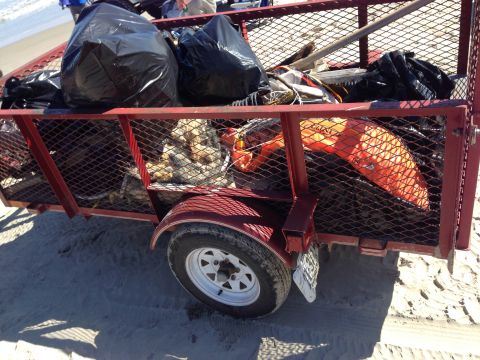 1979 Ford Bronco - A trailer loaded with trash bags and debris sits on a sandy beach, likely after a cleanup event.