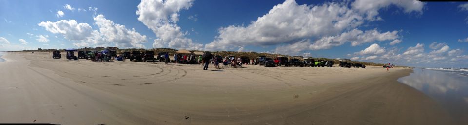 many off-road vehicles parked on a sandy beach with people around and the ocean in the background