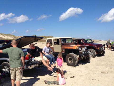 1979 Ford Bronco - A group of people relax on the beach next to a Jeep CJ-7 Renegade and a Ford pickup truck.