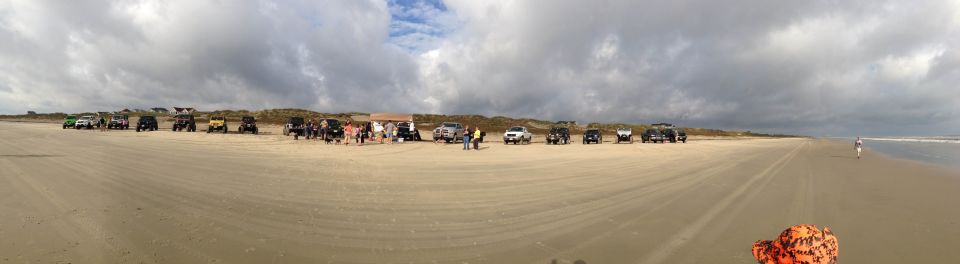 Group of off-road vehicles parked on a sandy beach with dunes and cloudy sky