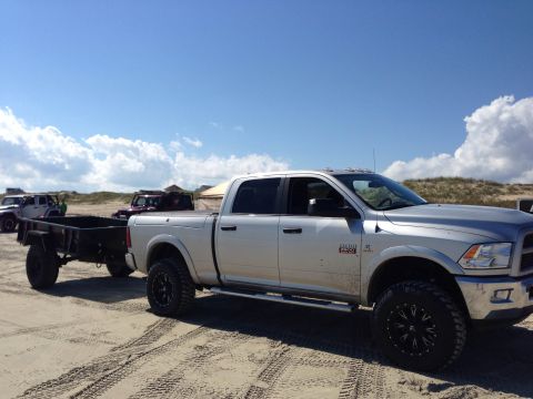 1979 Ford Bronco - A silver pickup truck tows a trailer across a sandy beach under a partly cloudy sky.