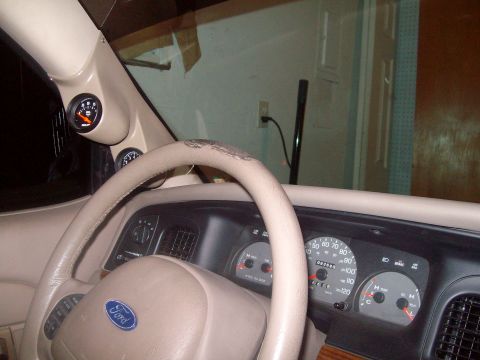 2004 Ford Crown Victoria - The dashboard of a car shows a Ford steering wheel and a cluster of gauges, including a voltmeter and oil pressure gauge.