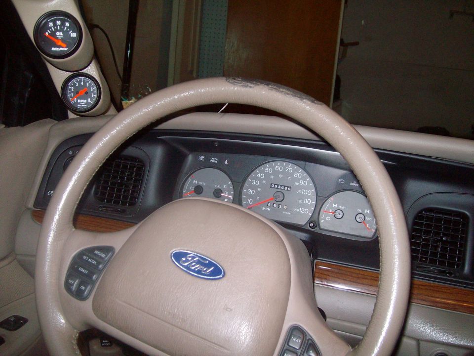 Tan steering wheel and dashboard of a 2003 Ford Crown Victoria with aftermarket gauges