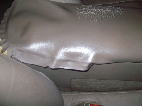 2004 Ford Crown Victoria - Close-up of a gray leather seat bolster showing significant cracking and peeling on the side bolster of a vehicle seat.