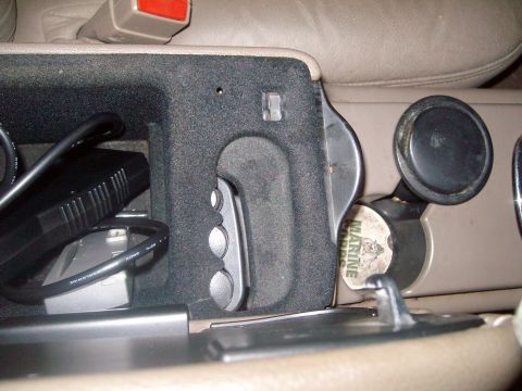 2004 Ford Crown Victoria - Open center console of a vehicle holding cables and a remote, with cup holders and a coin to the right.