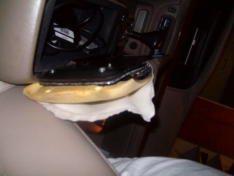 2004 Ford Crown Victoria - Open fold-out cup holder in a tan vehicle dashboard near the console shifter, with a cloth draped below.