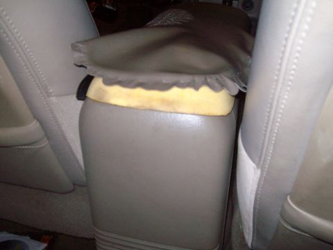 2004 Ford Crown Victoria - Tan leather center console armrest partly lifted to show yellow foam padding, between two matching tan leather seats.