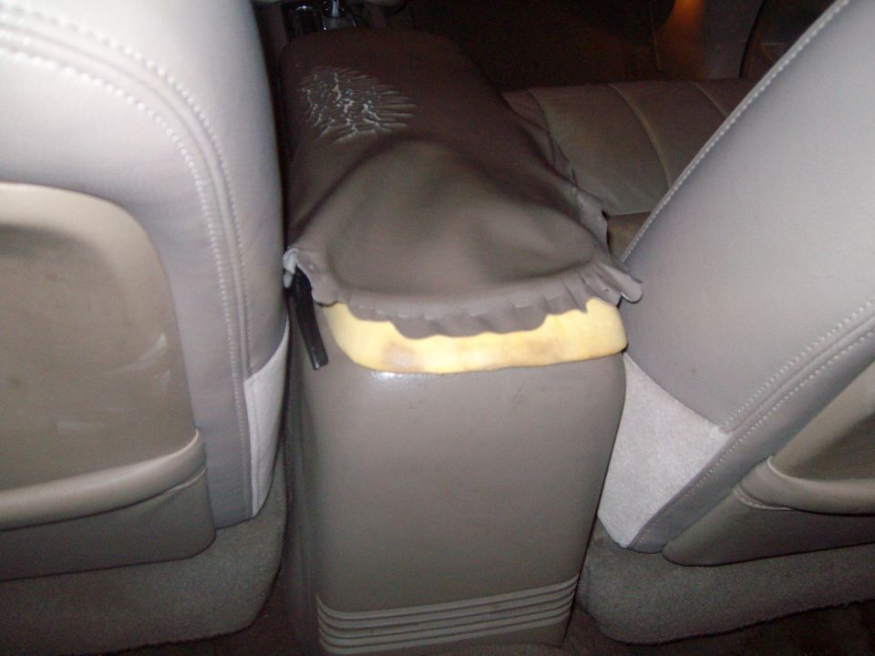 Center console with torn upholstery and exposed foam, between tan leather seats
