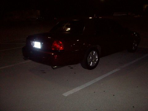 2004 Ford Crown Victoria - A dark-colored sedan is parked in a lot at night, viewed from the rear. The taillights and license plate area are illuminated.