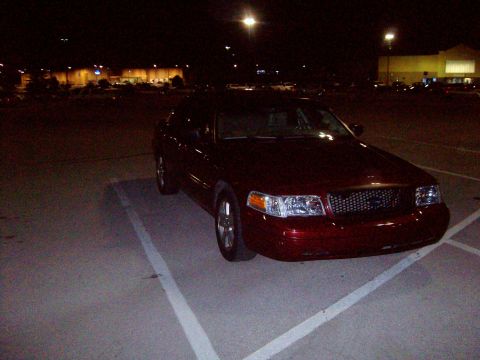 2004 Ford Crown Victoria - A red 2004 Ford Crown Victoria is parked in a lot at night, with a store in the background.