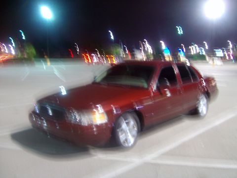 2004 Ford Crown Victoria - A red 2004 Ford Crown Victoria sedan is parked at night, with blurred lights in the background.