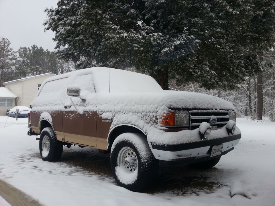 1991 Ford Bronco covered in snow, parked in a driveway