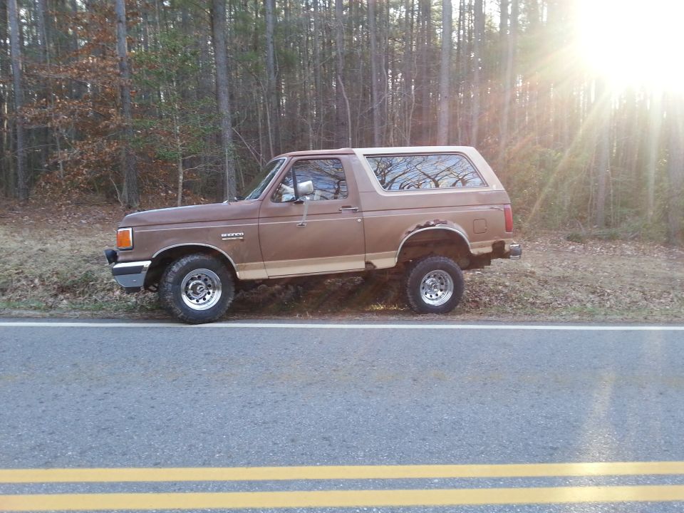 Brown Ford Bronco parked on the side of a road with trees in the background