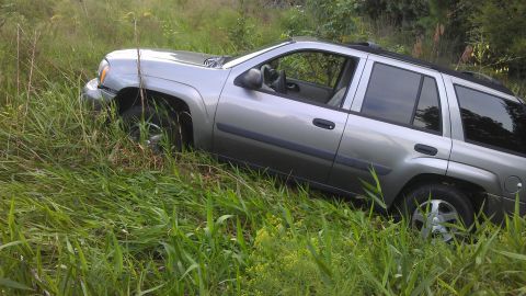 1994 Ford Bronco - Silver SUV is stuck in tall grass, with its front left wheel turned. The vehicle appears to be off-road.