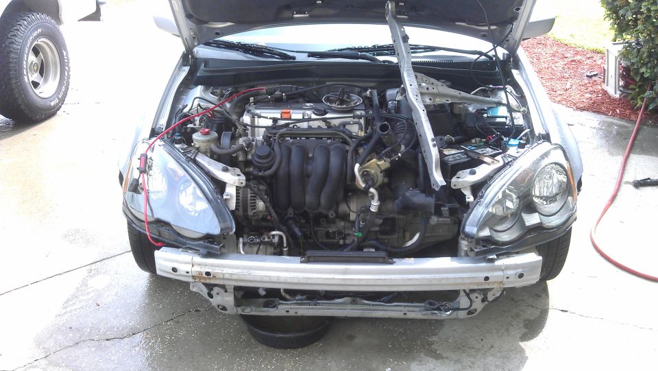 Car engine bay with front bumper removed, showing engine components and wiring