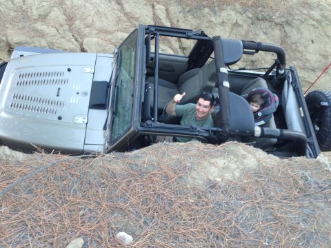 2005 Jeep Wrangler - Man and child in a Jeep Wrangler that has tipped onto its side on a rocky trail.