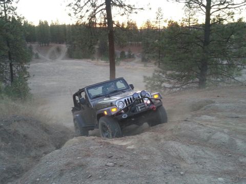 2005 Jeep Wrangler - A Jeep Wrangler navigates an off-road trail with trees and hills in the background.