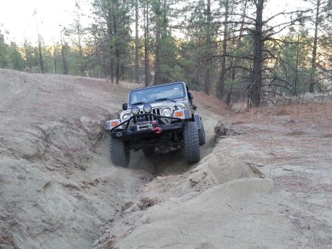2005 Jeep Wrangler - A silver 2005 Jeep Wrangler navigates a steep, sandy off-road trail with trees in the background.